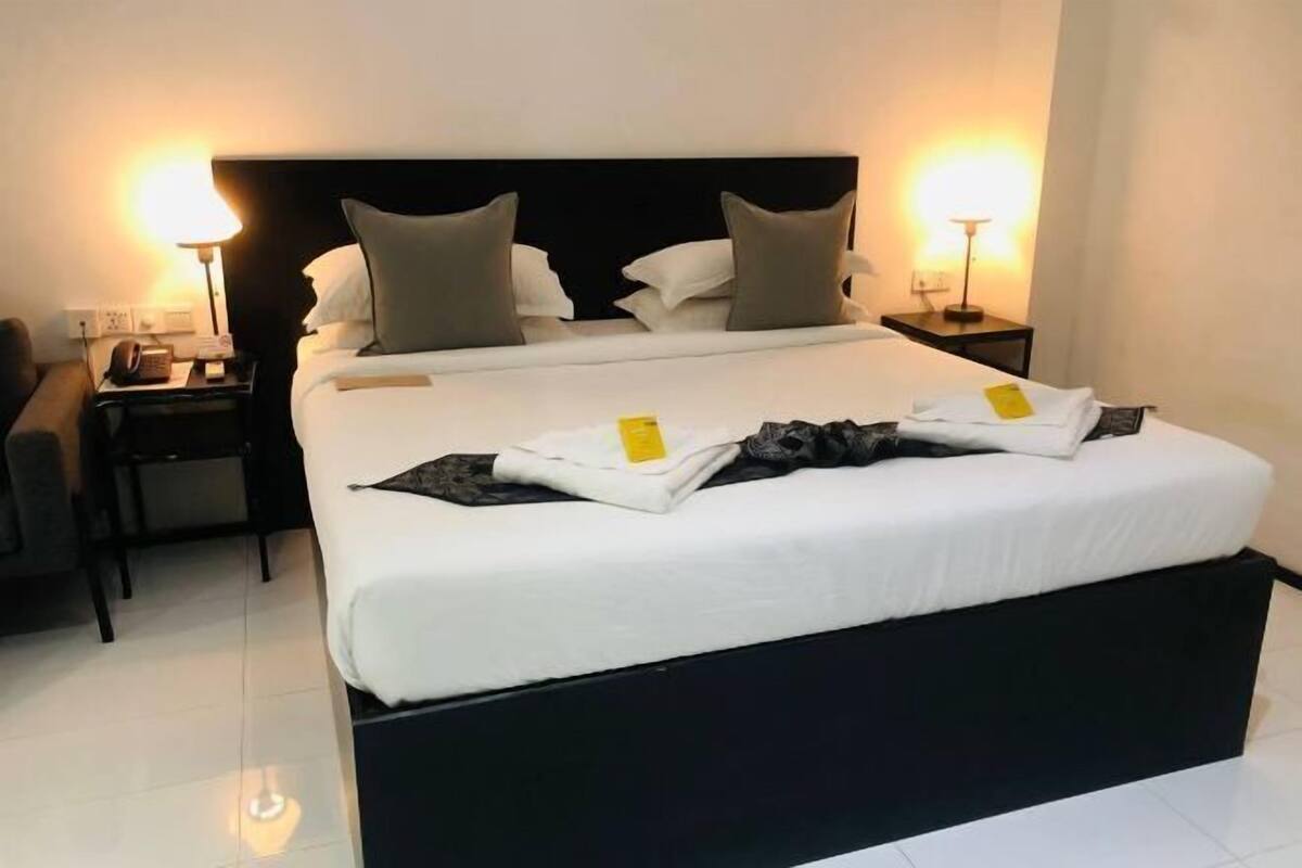 A hotel room with a large bed, two bedside tables, a chair, and two wall-mounted lamps.