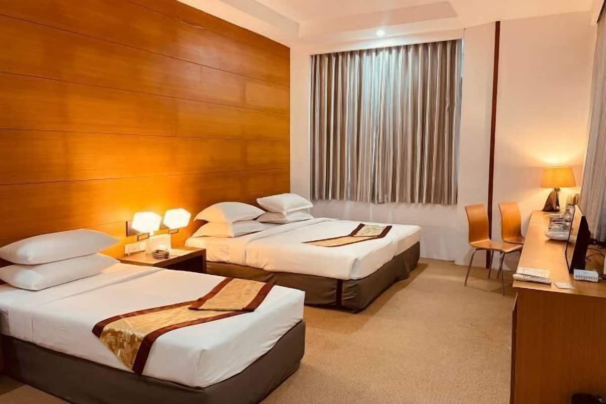 A hotel room with two beds, a desk, a chair, and a large window with curtains.