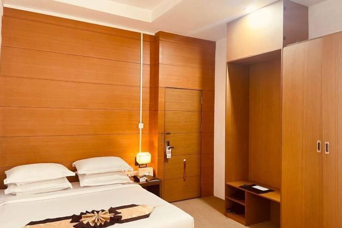 A hotel room with a bed, bedside table, lamp, wardrobe, and built-in shelving.