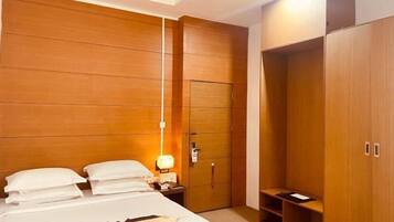 A hotel room with a bed, bedside table, lamp, wardrobe, and built-in shelving.
