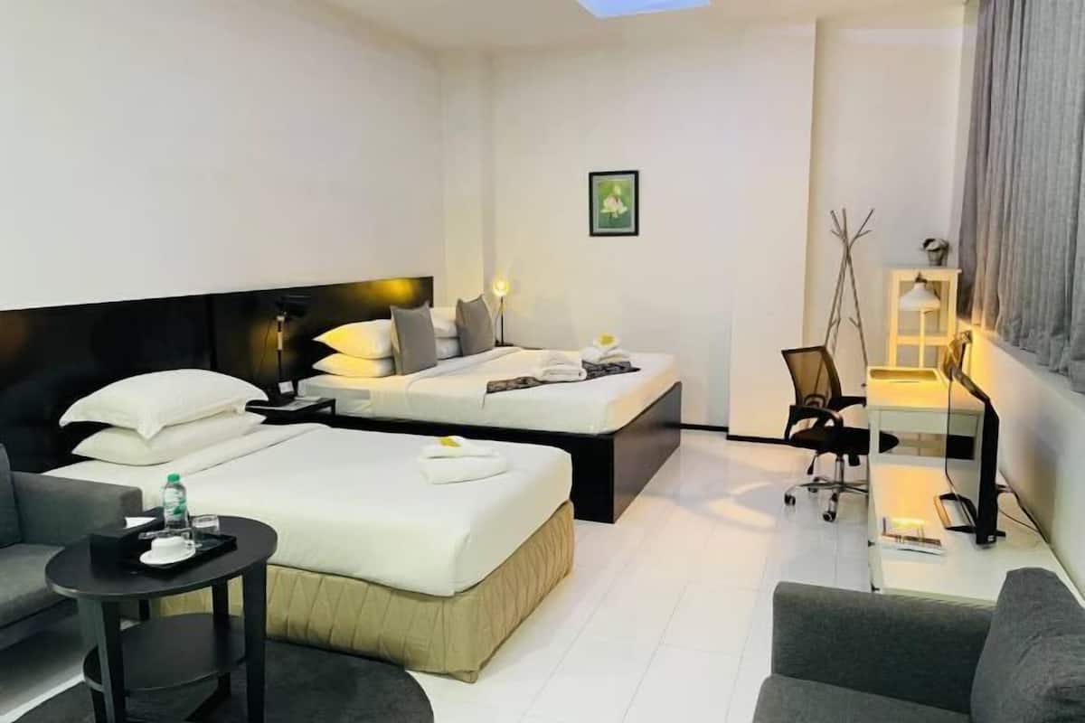 A modern hotel room with two beds, a desk, a chair, and a small table.