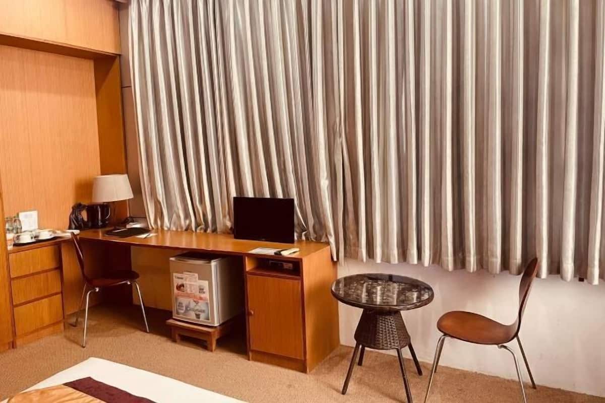 A hotel room with a wooden desk, a television, a small refrigerator, a coffee maker, a lamp, a round table, and a chair.