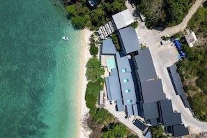 An aerial view of a coastal property with multiple buildings, a beach, and a boat. - The Hideout Beachfront (Phuket)