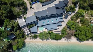 Vista aerea di un resort con diversi edifici, una spiaggia e un pontile per barche.