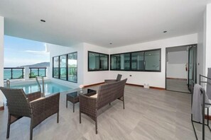 A modern room with a pool, wicker furniture, and large windows offering a view of the sea. - The Hideout Beachfront (Phuket)