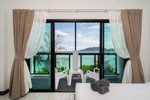 A hotel room with a bed, a view of the sea, and a balcony with chairs. - The Hideout Beachfront (Phuket)