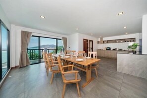 A spacious dining area with a large table and chairs, a kitchen area with modern appliances, and a balcony with a view of the sea.