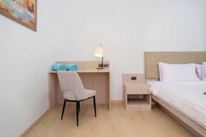 A bedroom with a bed, a desk with a chair, a nightstand, and a lamp. - The Hideout Beachfront (Phuket)