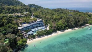 Una località balneare con un grande edificio, spiaggia e vegetazione rigogliosa.