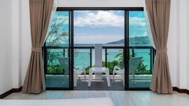 Una stanza con un'ampia porta-finestra scorrevole che dà su un balcone con vista sul mare e una sedia.