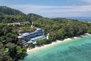 An aerial view of a coastal property with a beach, a boat, and a building surrounded by trees. - The Hideout Beachfront (Phuket)