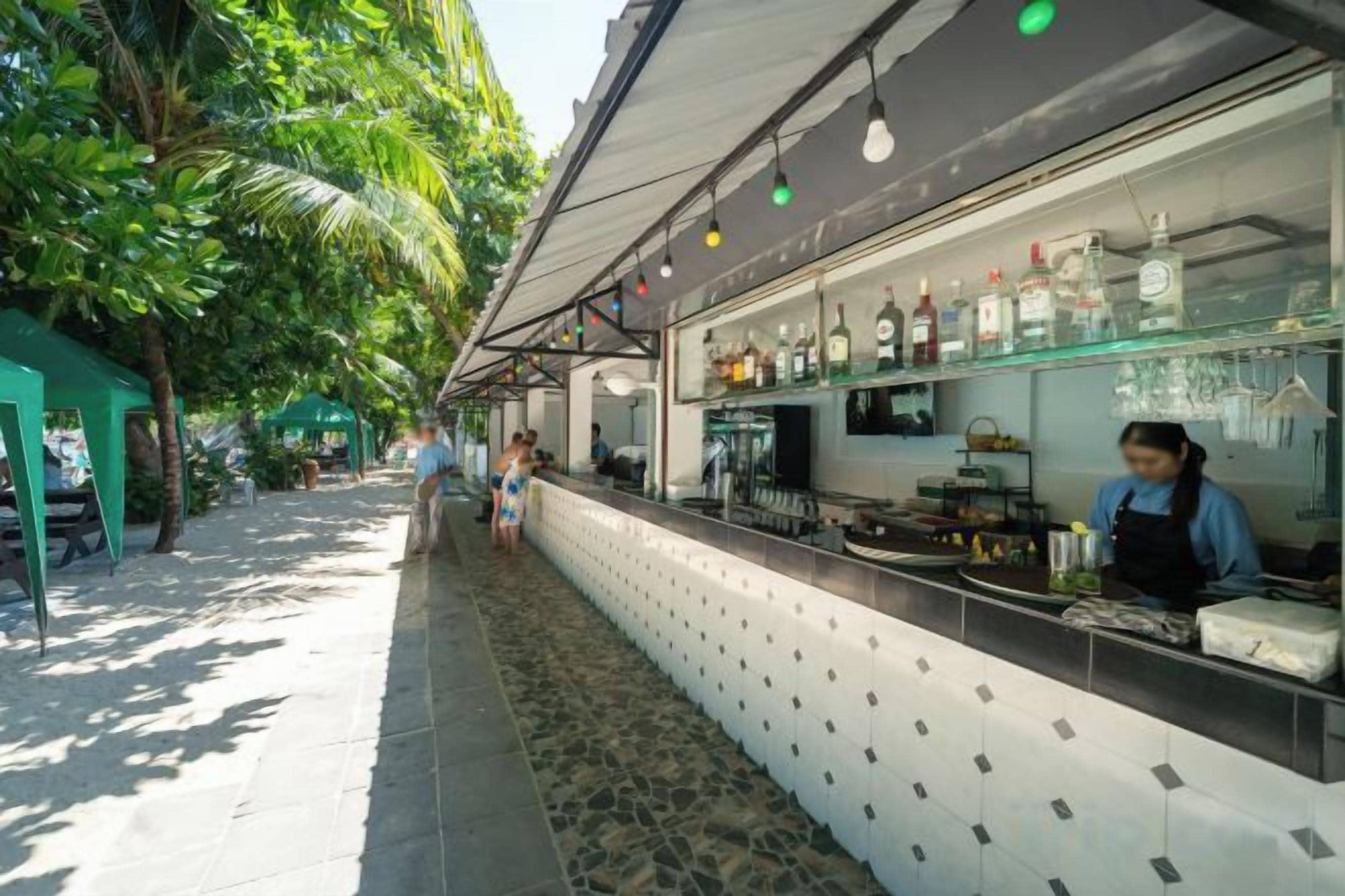 A bar area with a counter, shelves with bottles, and a person working behind the bar.
