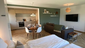 Un salon moderne comprenant un canapé, deux lits, un coin repas avec des chaises, une cuisine et un téléviseur fixé au mur.