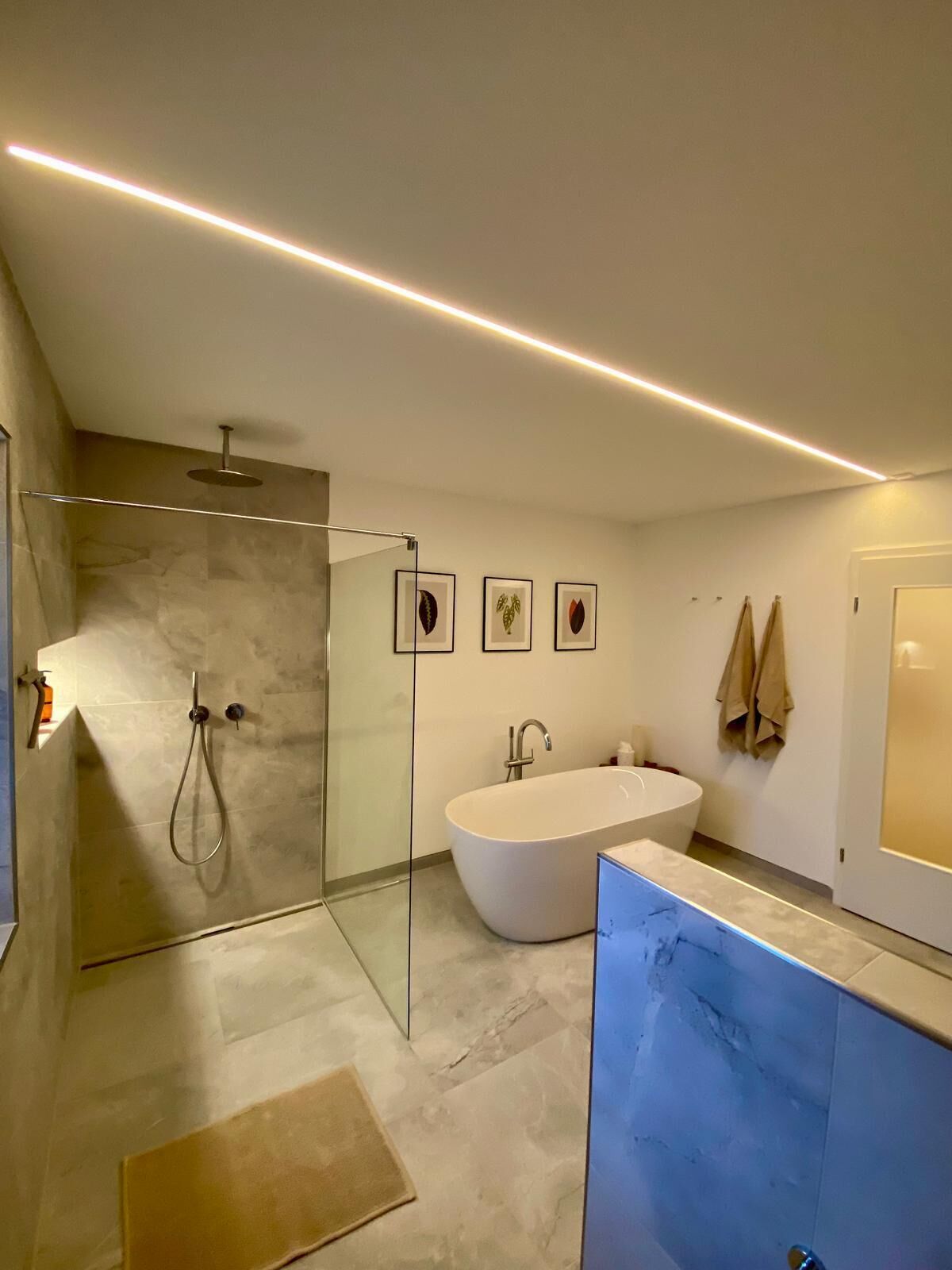 Een moderne badkamer met een glazen douchecabine, een vrijstaand bad en een wastafel met een marmeren aanrechtblad.