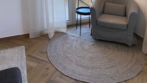 Une pièce avec un fauteuil gris, un petit tapis rond, un lampadaire et une porte-fenêtre coulissante donnant sur un espace extérieur.