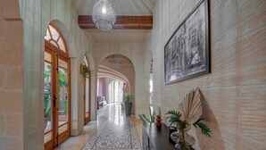 Un vaste hall d’entrée avec des portes en arc de cercle, un tapis à motifs et un luminaire suspendu.