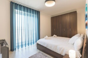 A modern bedroom with a large bed, wooden wardrobe, and a window with blue curtains. - Property with Pool access - Xaghra near Marsalforn (Xagħra)
