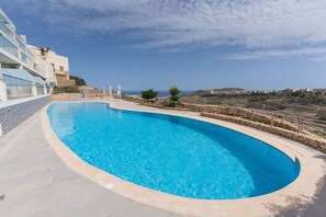 A curved swimming pool with a stone border, surrounded by a stone wall and a metal fence. - Property with Pool access - Xaghra near Marsalforn (Xagħra)