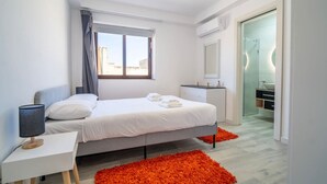 Une chambre à coucher moderne, avec un lit, une table de chevet et une salle de bain visible à travers une porte ouverte.