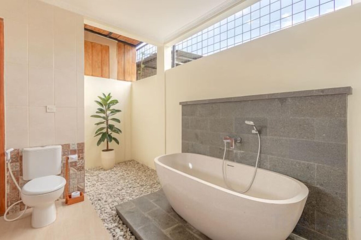 A bathroom with a freestanding bathtub, a toilet, and a potted plant.