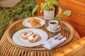Une table en osier avec un plateau en verre, deux assiettes de nourriture, une tasse de café et une serviette.