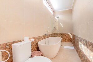 A modern bathroom with a freestanding bathtub, a toilet, and a shower area. - Anartha Resort Jimbaran By Kubu Gwk (Jimbaran)