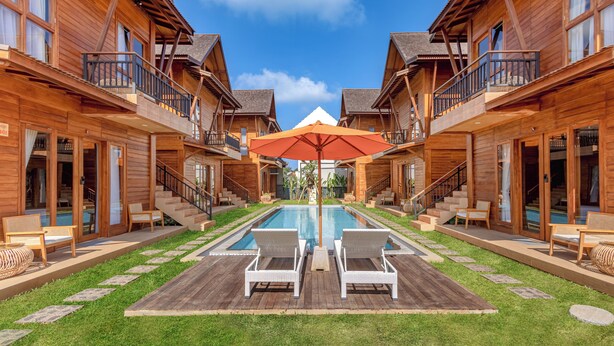 Un hôtel de style chalet en bois doté d’une piscine centrale, d’un espace extérieur aménagé et offrant une vue sur un ciel d’un bleu éclatant.