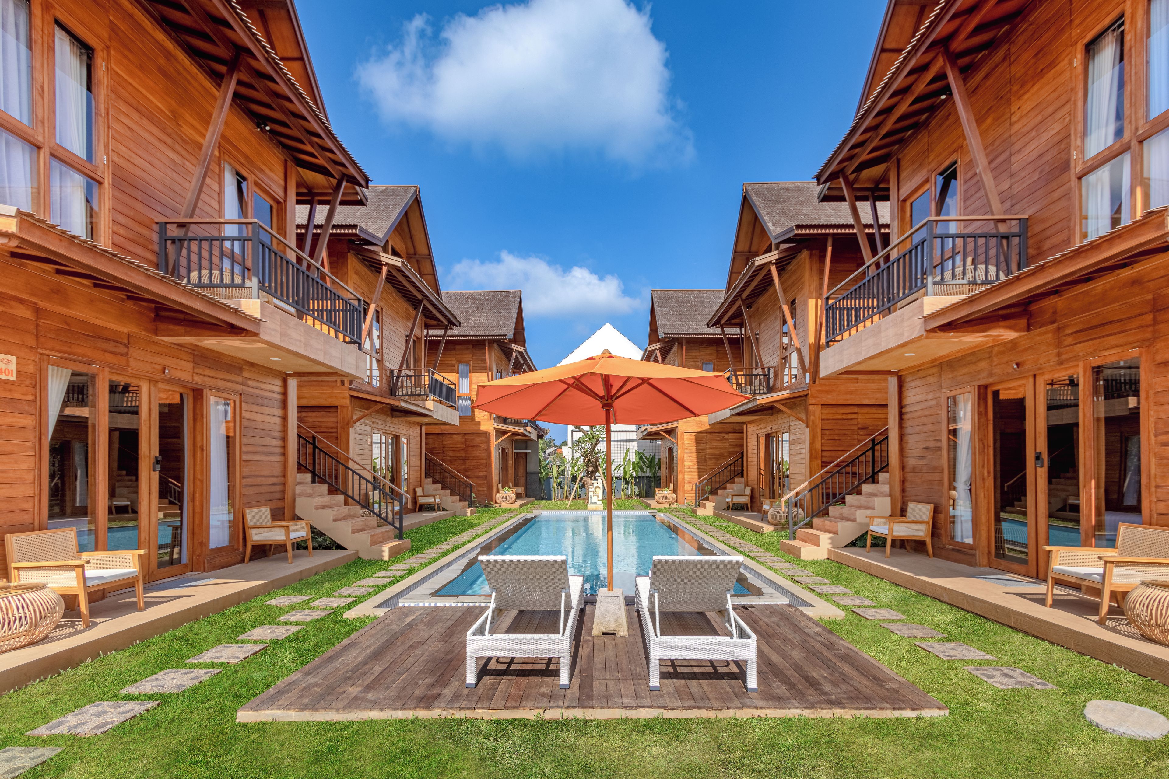 Un hotel tipo cabaña de madera con piscina central, mobiliario exterior y un cielo azul despejado.