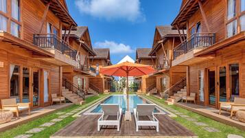 A wooden cabin-style hotel with a central pool, outdoor seating, and a clear blue sky.