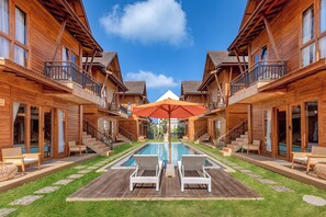 Un hôtel de style chalet en bois doté d’une piscine centrale, d’un espace extérieur aménagé et offrant une vue sur un ciel d’un bleu éclatant.