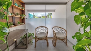 A small, modern room with two wicker chairs, a wooden table, and shelves with potted plants.