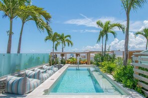 Zona de piscina con mobiliario de relax y palmeras.