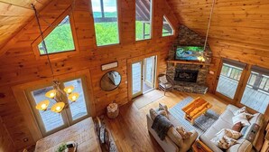 A spacious loft-style room with a stone fireplace, large windows, and a cozy seating area. - NEW-Mountian Views! Hot Tub-Game Room-Near Town (Blue Ridge)