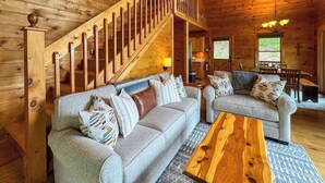 A cozy log cabin interior with a staircase, two sofas, a wooden coffee table, and a cross on the wall. - NEW-Mountian Views! Hot Tub-Game Room-Near Town (Blue Ridge)