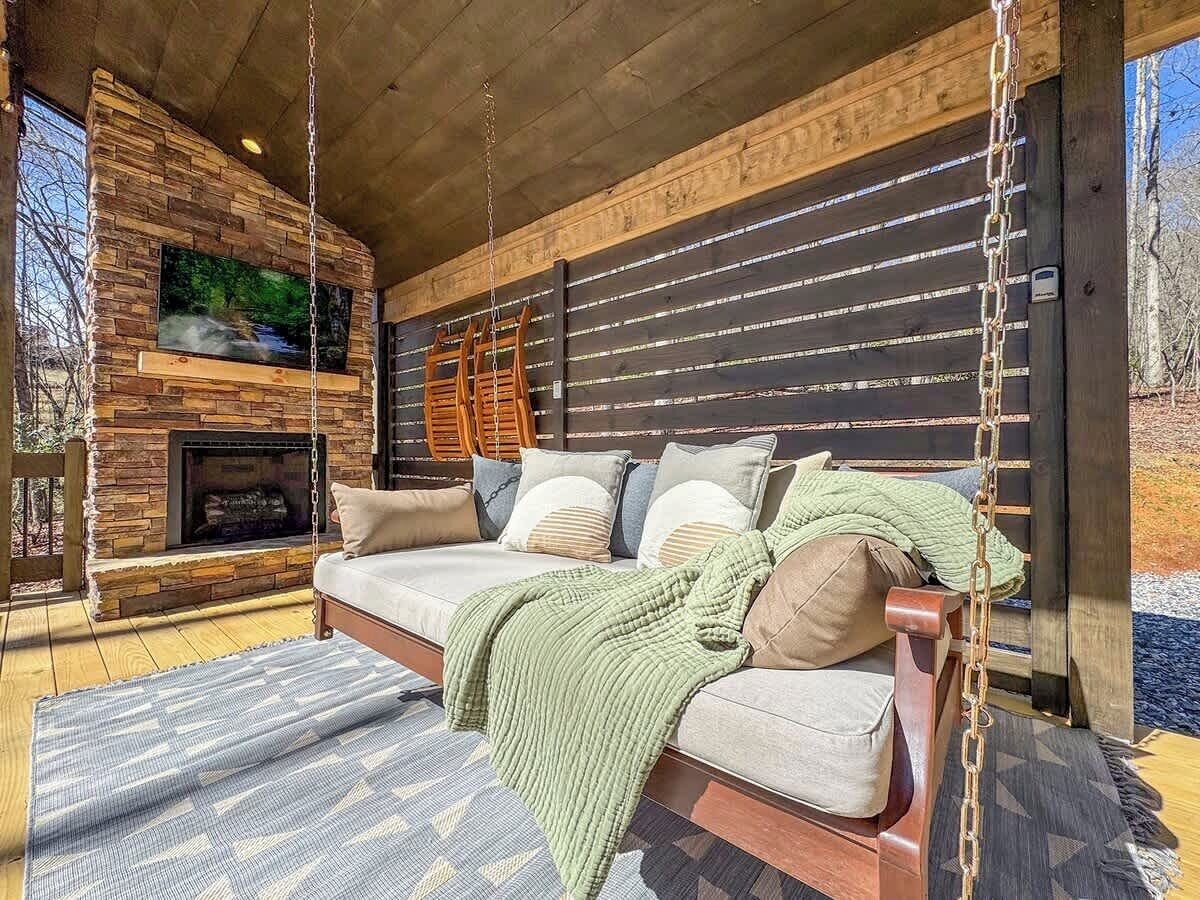 A cozy outdoor seating area with a stone fireplace, a swing, and a cushioned sofa.