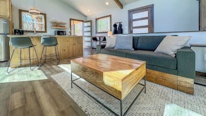 Una sala de estar moderna con una mesa de centro de madera, un sofá y una zona de cocina con taburetes de bar.