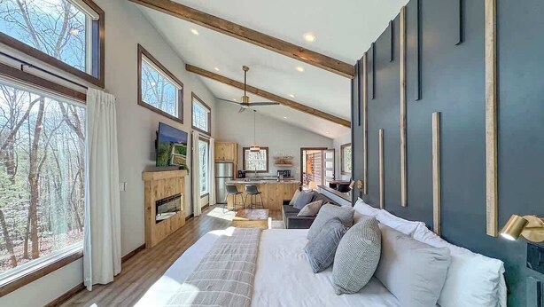 Un dormitorio moderno con una cama grande, cabecera de madera y vistas al bosque a través de amplios ventanales.