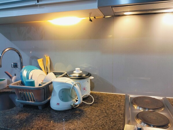 Una cocina con un lavabo, escurreplatos, hervidor y estufa.