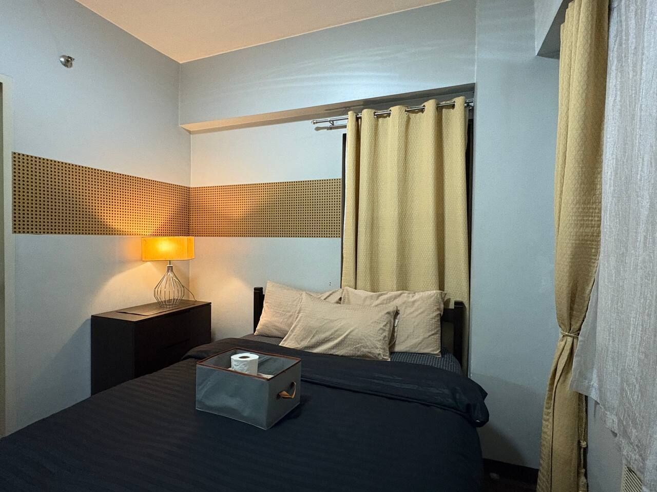 A hotel room with a bed, a nightstand, a lamp, and curtains.