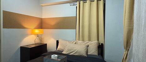 A hotel room with a bed, a nightstand, a lamp, and curtains.