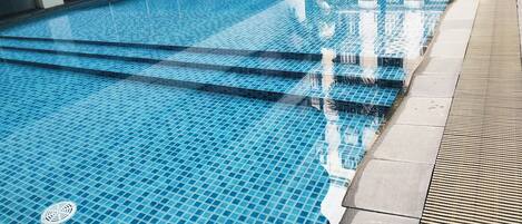 A swimming pool with clear blue tiles, steps leading into the water, and a tiled walkway beside it.