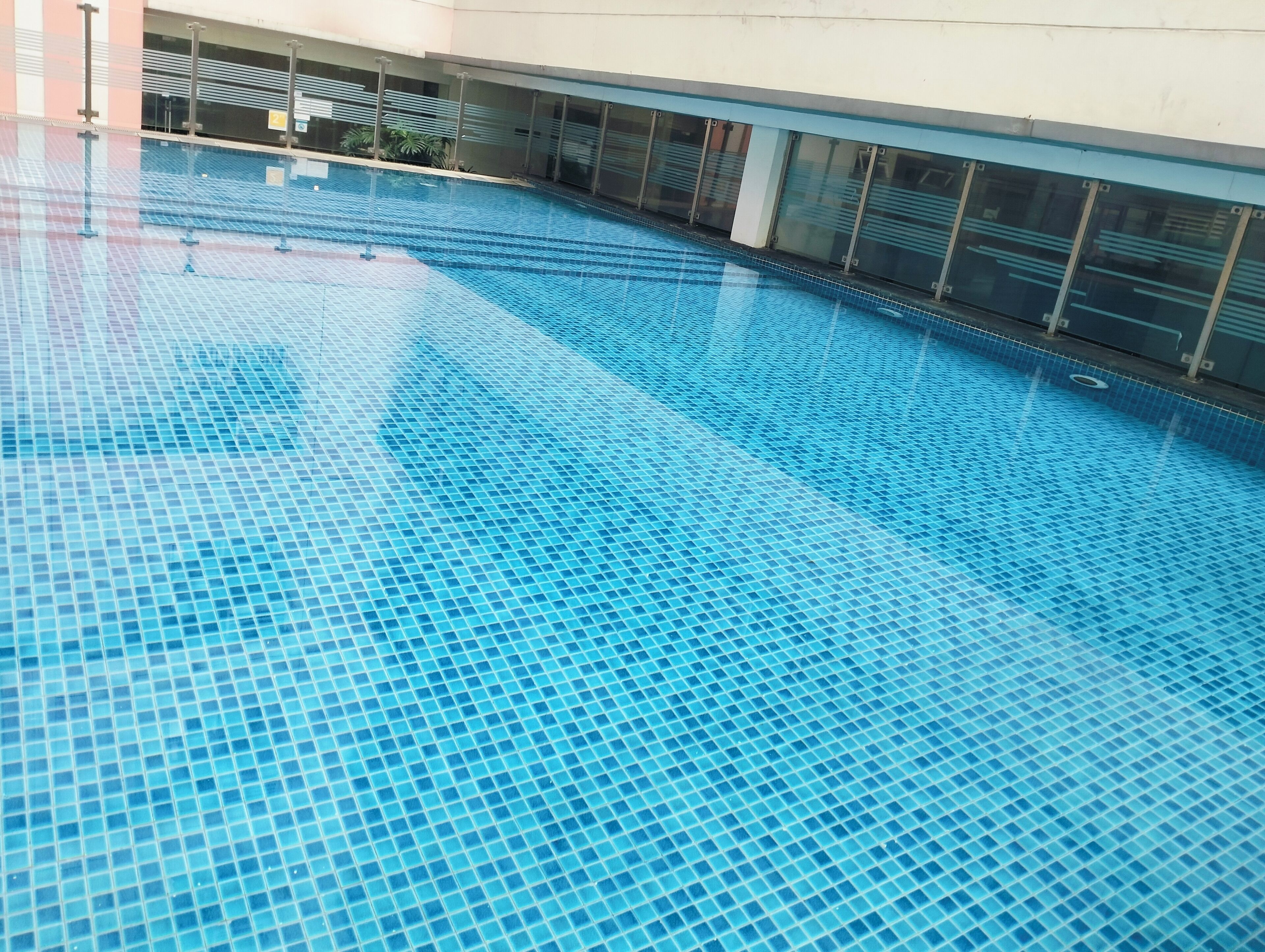 A large indoor swimming pool with clear blue water, surrounded by a modern building with large windows and a tiled floor.
