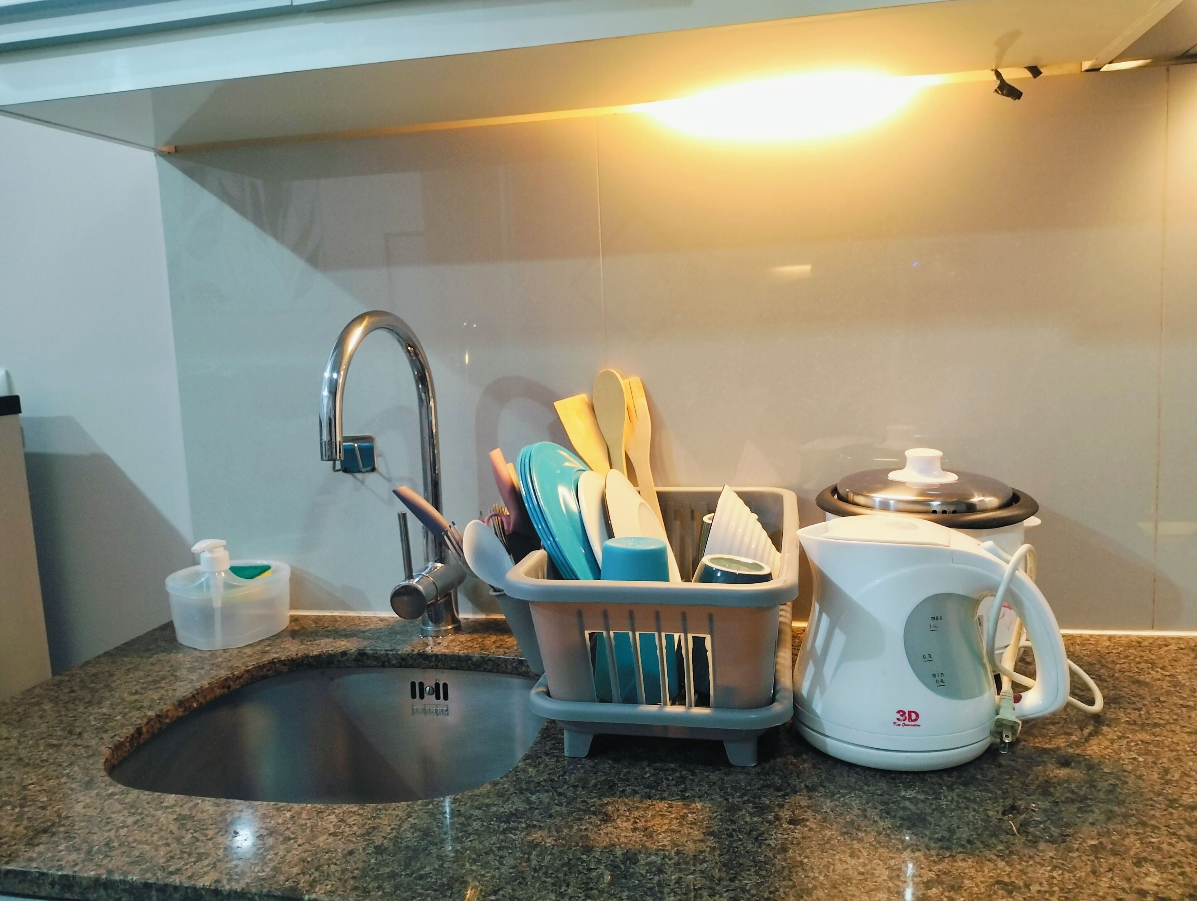 Eine Küche mit Spüle aus Edelstahl, einem Geschirrgestell mit Besteck und einem weißen Wasserkocher.