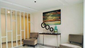 A modern room with a white tiled floor, a beige patterned sofa, a small table with decorative items, and a colorful abstract painting on the wall. - NAIA MNL Airport-Newport Accommodations (Pasay)