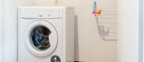 A laundry room with a washing machine, a shelf with cleaning supplies, and a window with a towel rack.