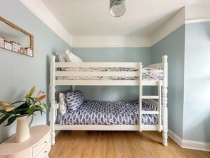 A bunk bed with patterned bedding, a vase with flowers, and a wooden floor.