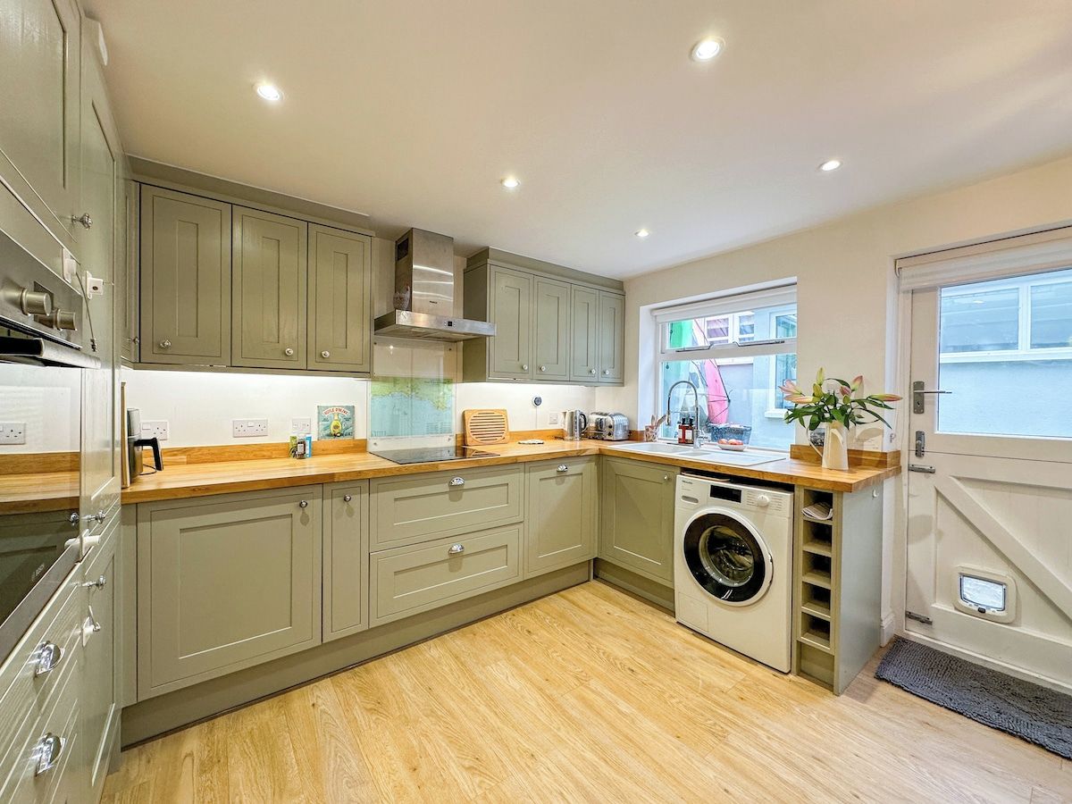 A modern kitchen with built-in appliances, a washing machine, and a window with a view.