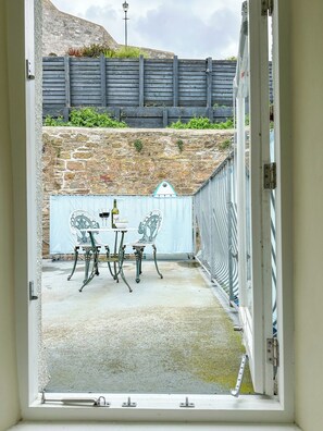 An open doorway to a patio area with a stone wall, a metal fence, and a table with chairs.