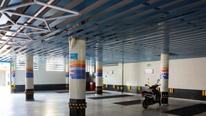 An indoor parking area with multiple columns, a motorcycle parked, and a ceiling with blue beams. - Hotel Puerto Angel (Nezahualcóyotl)