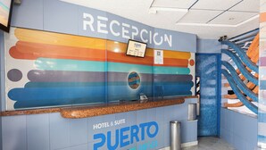 A reception area with a colorful wall design, a sign for Puerto Angel, and a metal trash can. - Hotel Puerto Angel (Nezahualcóyotl)